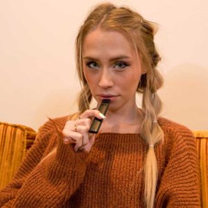 Attractive blonde woman wearing an orange sweater holding a black CCell Slym disposable cannabis vape.
